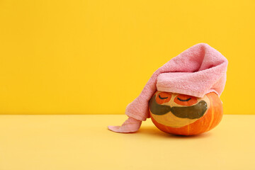 Funny pumpkin with cosmetic mask, under-eye patches and towel on color background
