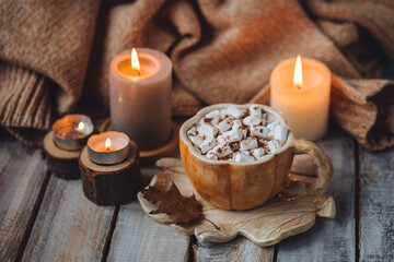 Spicy sweet fall hot drink: delicious pumpkin latte with cinnamon, marshmallow with salted caramel. Served in handmade artisan mug in shape of pumpkins, cozy home decor with candles, dry autumn leaves