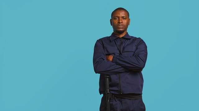 Security guard does surveillance for various organizations and venues, ensuring protection of property and personnel, studio background. Portrait of intimidating man in uniform crossing arms, camera B