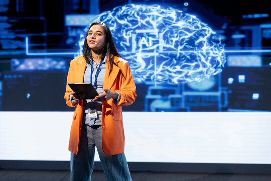 Happy executive holding tablet speaking at event bringing together leading researchers to explore developments in AI and machine learning. Jolly engineer using device to hold tech presentation