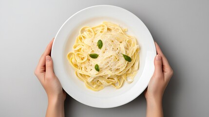 A person is holding a plate of pasta with a green leaf on top