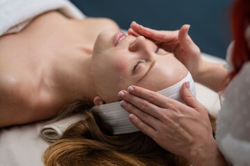 Spa woman applying facial clay mask, close up. Beauty skin massage in a beauty clinic. Facial lifting in SPA salon. A cosmetologist girl does a facial massage. Cosmetic procedure. Beauty cosmetology.