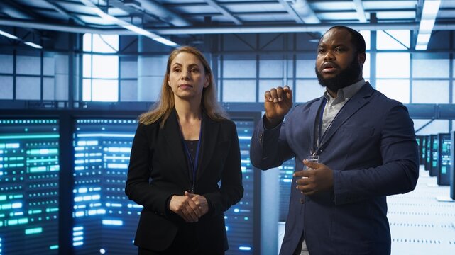 Teamworking technicians in high tech data center workspace looking at hologram visualization. Programmer and colleague working on securing server room hardware using AR tech, camera A
