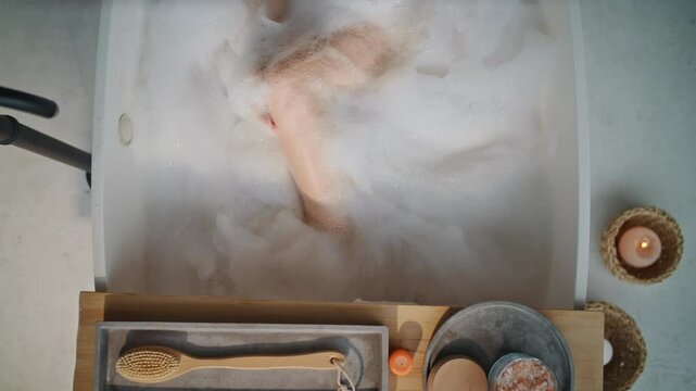 Beautiful woman soaking bath filled by white fluffy foam feeling serene top view