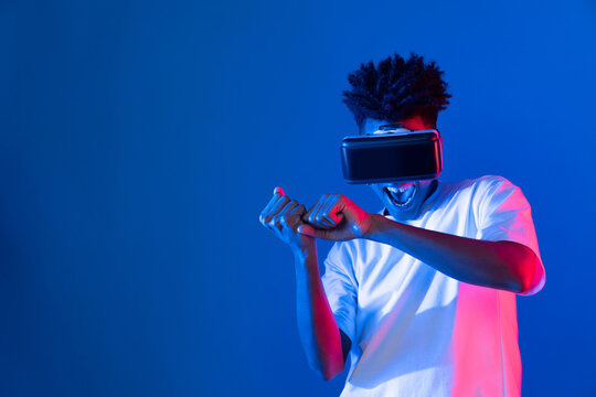 Young African American player wearing VR playing sword or baseball hologram isolated blue pink neon lighting wall connecting digital futuristic technology virtual reality metaverse world. Contrivance.
