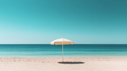 Fototapeta premium A wide shot of a sandy beach with a single beach umbrella and a calm sea under a cloudless sky.