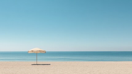 Fototapeta premium A wide shot of a sandy beach with a single beach umbrella and a calm sea under a cloudless sky.