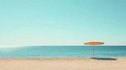 A wide shot of a sandy beach with a single beach umbrella and a calm sea under a cloudless sky.