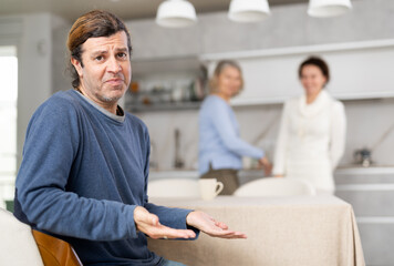 Fototapeta premium Distressed man is present during quarrel between his wife and elderly female mom. Mature woman and daughter-in-law swear and insult each other
