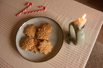 Merry Christmas! Gingerbread cookies lie in a plate on the table, there is a candle and lollipops. The background is a beautiful cozy home interior. Time for family