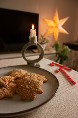 Merry Christmas! Gingerbread cookies lie in a plate on the table, there is a candle and lollipops. The background is a beautiful cozy home interior. Time for family