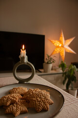 Merry Christmas! Hand holding gingerbread man cookie with icing on background of cookies in plate on table against christmas tree golden lights. Atmospheric Christmas holidays, family time