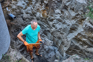 Homeowner prepares ditch for septic tank with his own hands, removing soil with bayonet shovel.