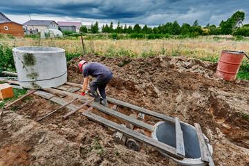 Worker moves concrete ring for septic tank along rollers made of steel pipes.