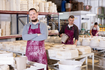 Portrait of smiling young bearded man, confident successful ceramicist, standing in stained maroon...