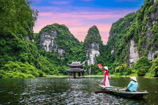 Vietnamese cultural clothing on a boat floating in the river flowing through the mountains at Trang An, Vietnam