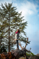 A fashionable woman stands on a log in front of a tree