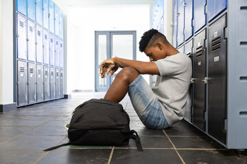 Sitting in school hallway, teenage boy leaning against lockers with backpack