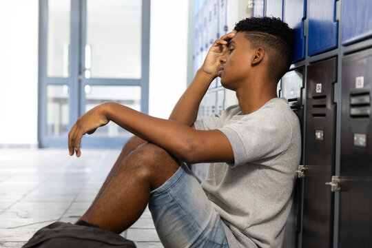 Sitting in school hallway, teenage boy leaning against lockers, looking stressed