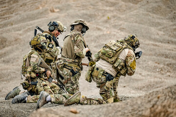 A group of military men in combat gear patrol in the middle of a desert and tropical jungle....