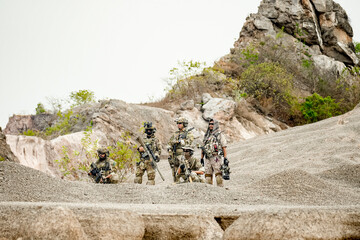 A group of military men in combat gear patrol in the middle of a desert and tropical jungle....