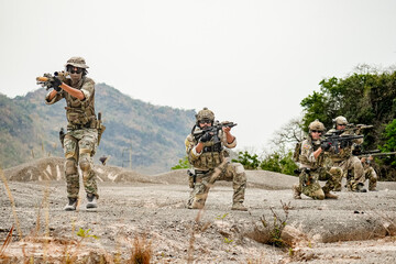 Fototapeta premium A group of military men in combat gear patrol in the middle of a desert and tropical jungle. Soldiers in full combat gear in dry weather conditions assemble and march on a mission.