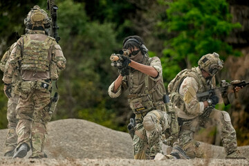 A group of military men in combat gear patrol in the middle of a desert and tropical jungle....
