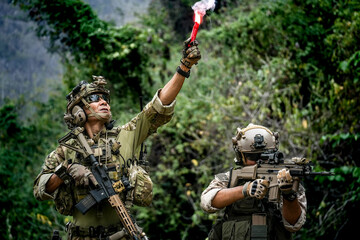 Two soldiers in tactical gear operate in a dense forest, one holding a flare and hold...