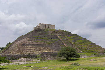 pyramid ruins in archaeological zone located in Queretaro, Mexico. Which is surrounded by nature and vegetation, with a cloudy sky which looks beautiful