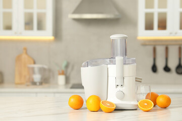 Modern juicer, oranges and glass on white marble table in kitchen, space for text