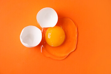 Broken raw egg and shell on orange background, top view
