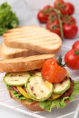 Tasty sandwich with grilled vegetables on white tiled table, closeup