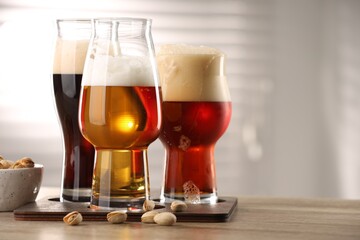 Glasses with different types of beer and pistachio nuts on wooden table indoors, closeup. Space for text