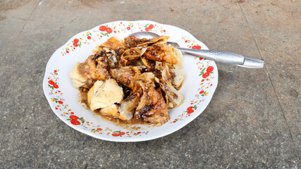 Close-up of Batagor, a traditional Indonesian street food from Bandung, served on a floral-patterned plate with peanut sauce and sweet soy sauce. A spoon rests beside the crispy fried dumplings