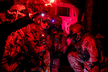 soldiers wearing combat gear gather around a flare during military operation. The dark setting and flare emphasize the stealth and readiness. soldiers using a red flare to strategize night mission.