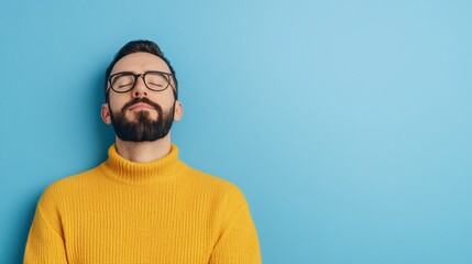 Fototapeta premium Young Middle-Eastern man in yellow sweater and glasses, relaxing against a blue background.