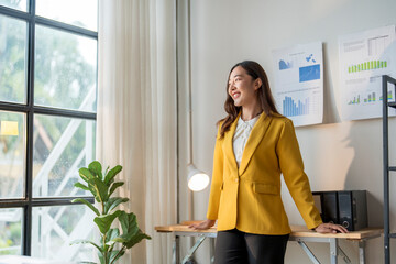 Young asian businesswoman leaning on desk and looking out window