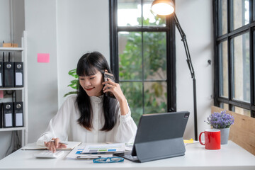 Asian accountant woman using calculator and talking on mobile phone at her office