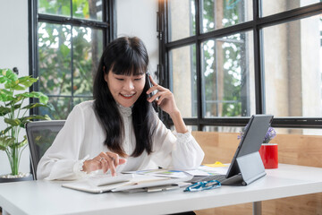 Asian accountant woman talking on phone and using calculator in office