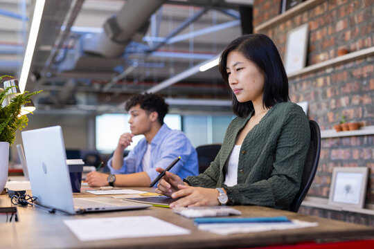 Working in modern office, asian woman using laptop and stylus for design work