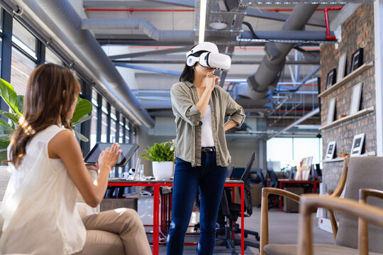 In office, Using VR headset, asian woman exploring virtual interior design while colleague observes