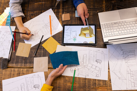 At office, diverse team using tablet, fabric samples, and sketches on table
