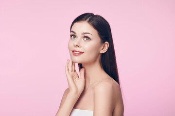 Beautiful young woman with glowing skin posing with her hands on her face against a pink background