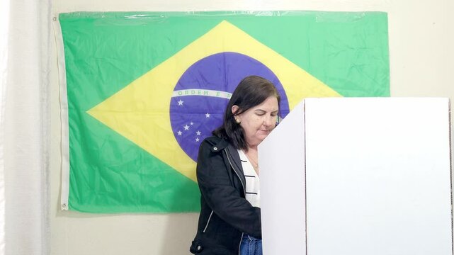 Eleitora mulher brasileira na cabine de vota&ccedil;&atilde;o escolhendo o seu candidato na urna eletr&ocirc;nica brasileira. Elei&ccedil;&otilde;es presidenciais e municipais no Brasil. No fundo, a bandeira do Brasil decora o local.