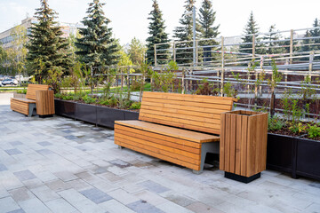 In a beautifully designed green space, there are modern wooden benches strategically set among stunning planters filled with abundant greenery