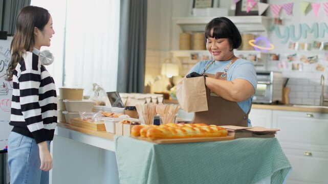 Young asian female customer using mobile phone to pay for paper bag full of freshly baked goods.NFC QR code device,payWave,contactless payment code for fast digital transaction.