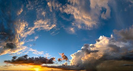 Colorful sunset sky with setting sun behind vivid orange and yellow clouds