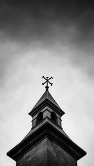 A striking black and white image showcasing the peak of a church steeple against a dynamic cloudy sky.