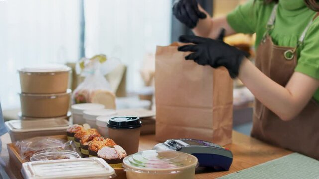 Young asian female customer using mobile phone to pay for paper bag full of freshly baked goods.NFC QR code device,payWave,contactless payment code for fast digital transaction.