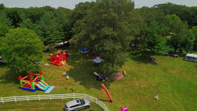 Aerial view of a lush green park area featuring colorful inflatable bounce houses and playground equipment, surrounded by trees and picnic spots for family enjoyment.
